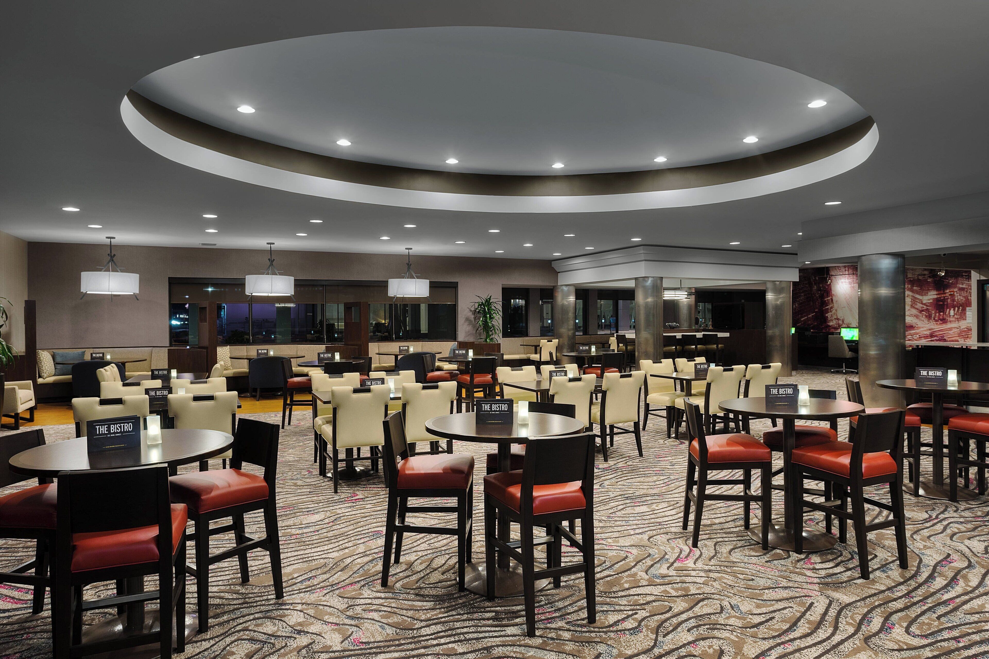 A hotel lobby with round tables and chairs, a central bar area, and a patterned carpet.