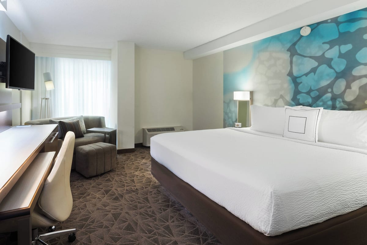 Une chambre d’hôtel dotée d’un grand lit, d’un bureau, d’une chaise, d’un téléviseur à écran plat et d’un mur orné d’un motif abstrait bleu.