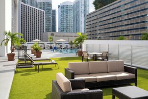 A rooftop terrace with a green lawn, outdoor seating, and a view of the Miami Convention Center.