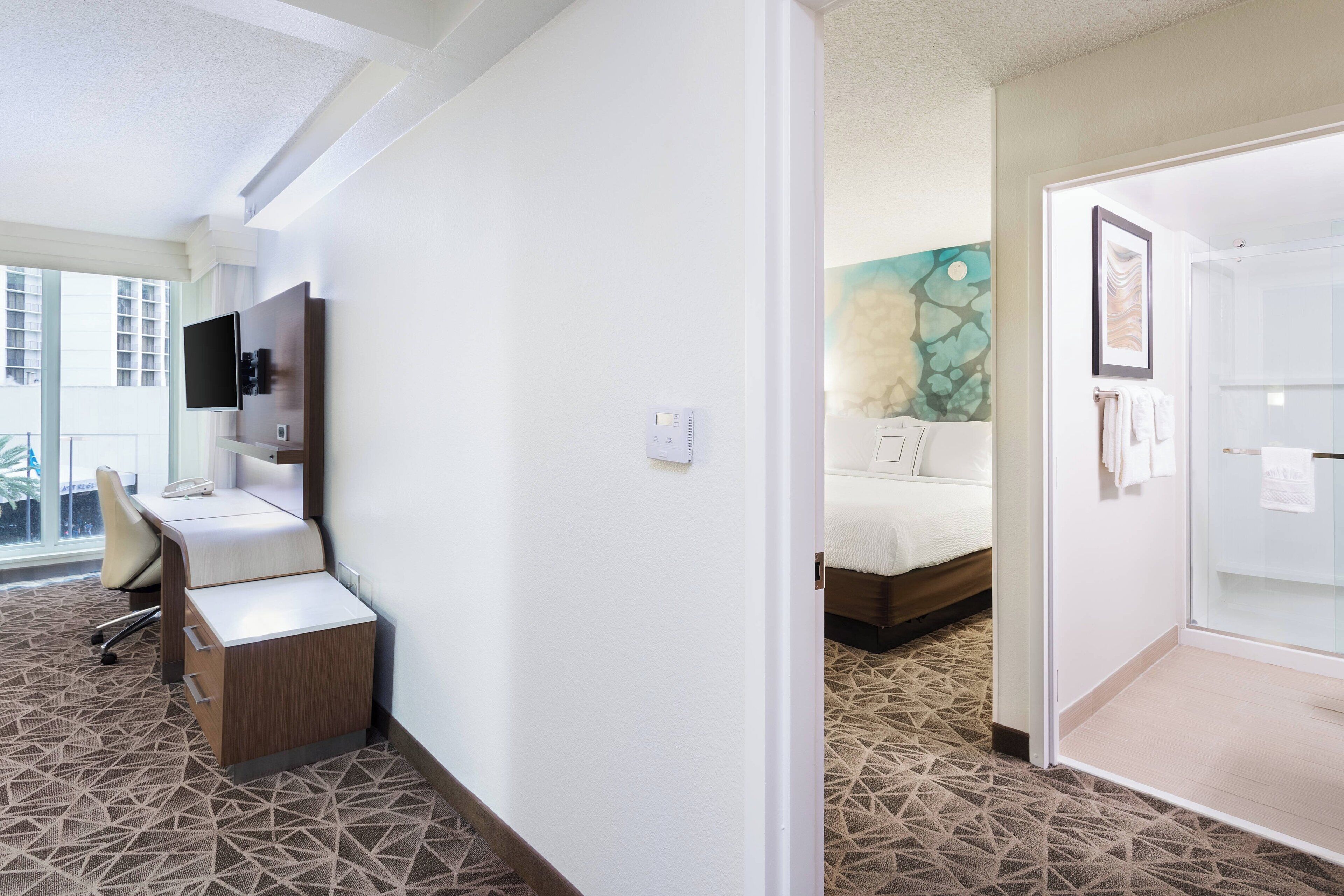 Een hotelkamer met een bureau, stoel, bed en een badkamer met douche.