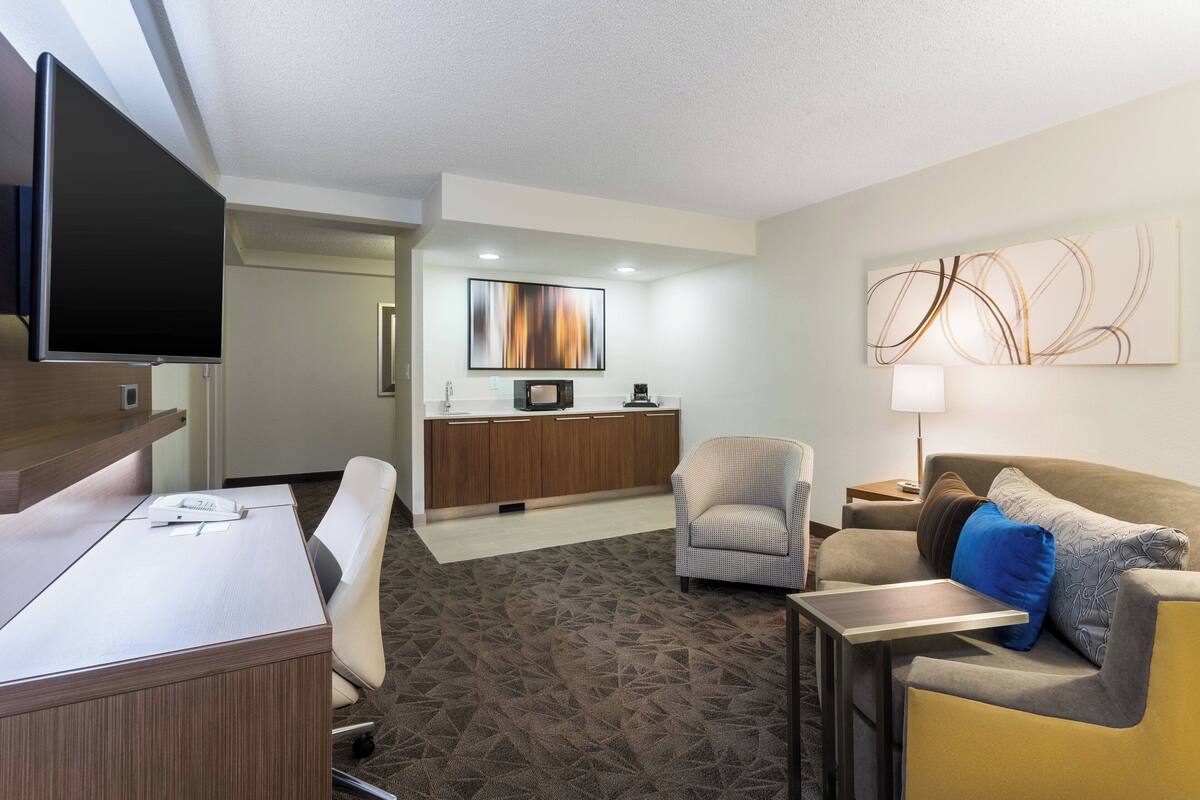 Une chambre d’hôtel équipée d’un bureau, d’un canapé, d’une chaise, d’une télévision, d’une machine à caf é et d’un tableau au mur.