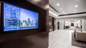 A hotel lobby with a large digital display showing local events and weather, a reception desk, and a seating area with a view of the cityscape. - Courtyard by Marriott Miami Downtown (Miami)