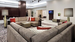 A modern hotel lobby with a sectional sofa, a coffee table, and a TV mounted on the wall. - Courtyard by Marriott Miami Downtown (Miami)
