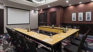 A conference room with a long table, chairs, a projector screen, and framed pictures on the wall.