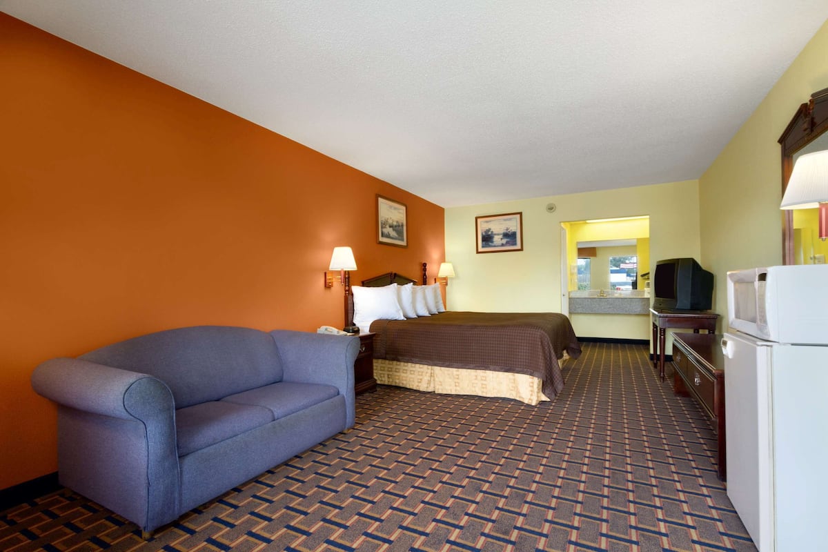 A hotel room with a sofa, a bed, a television, and a refrigerator.