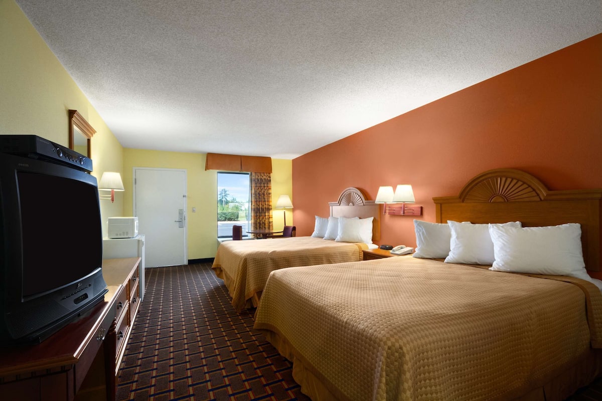 A hotel room with two beds, a television, a desk, and a window with a view.