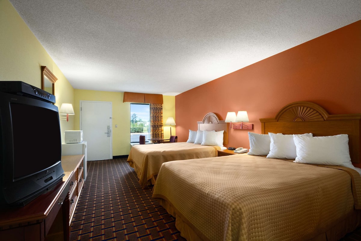 A hotel room with two beds, a television, a desk, and a window with a view.