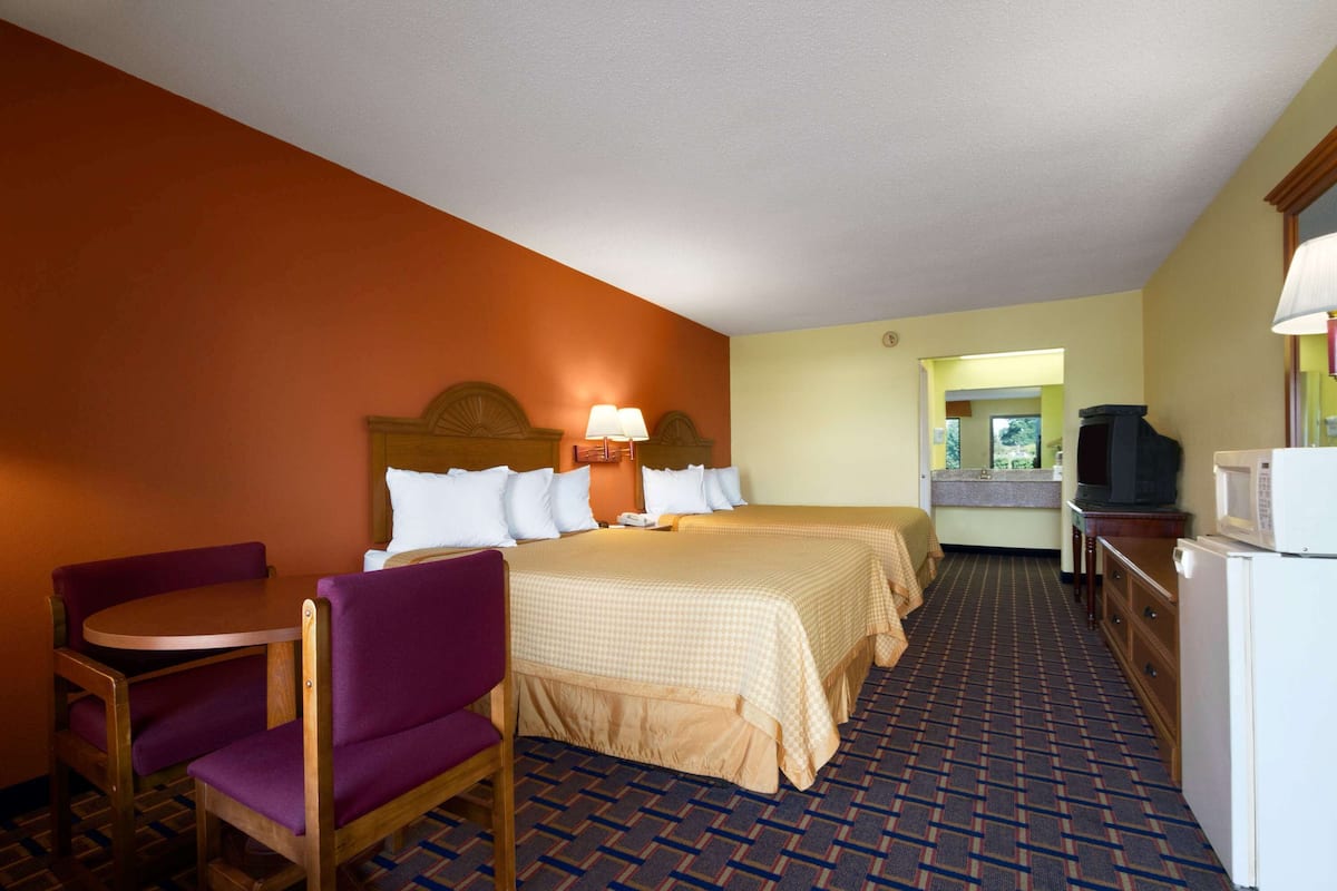 A hotel room with two beds, a dining table, a chair, a television, and a microwave.