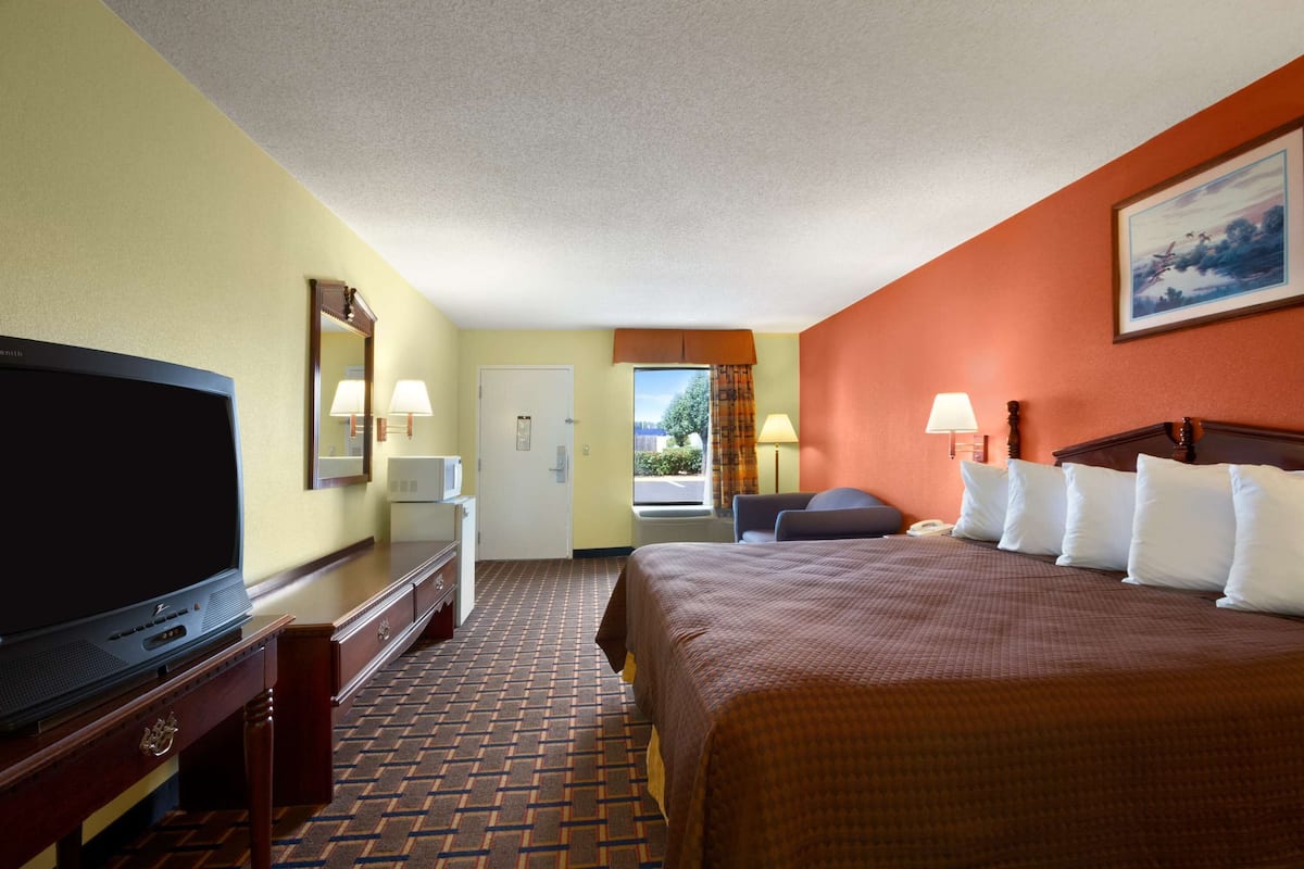 A hotel room with a bed, a television, a desk, and a window with curtains.