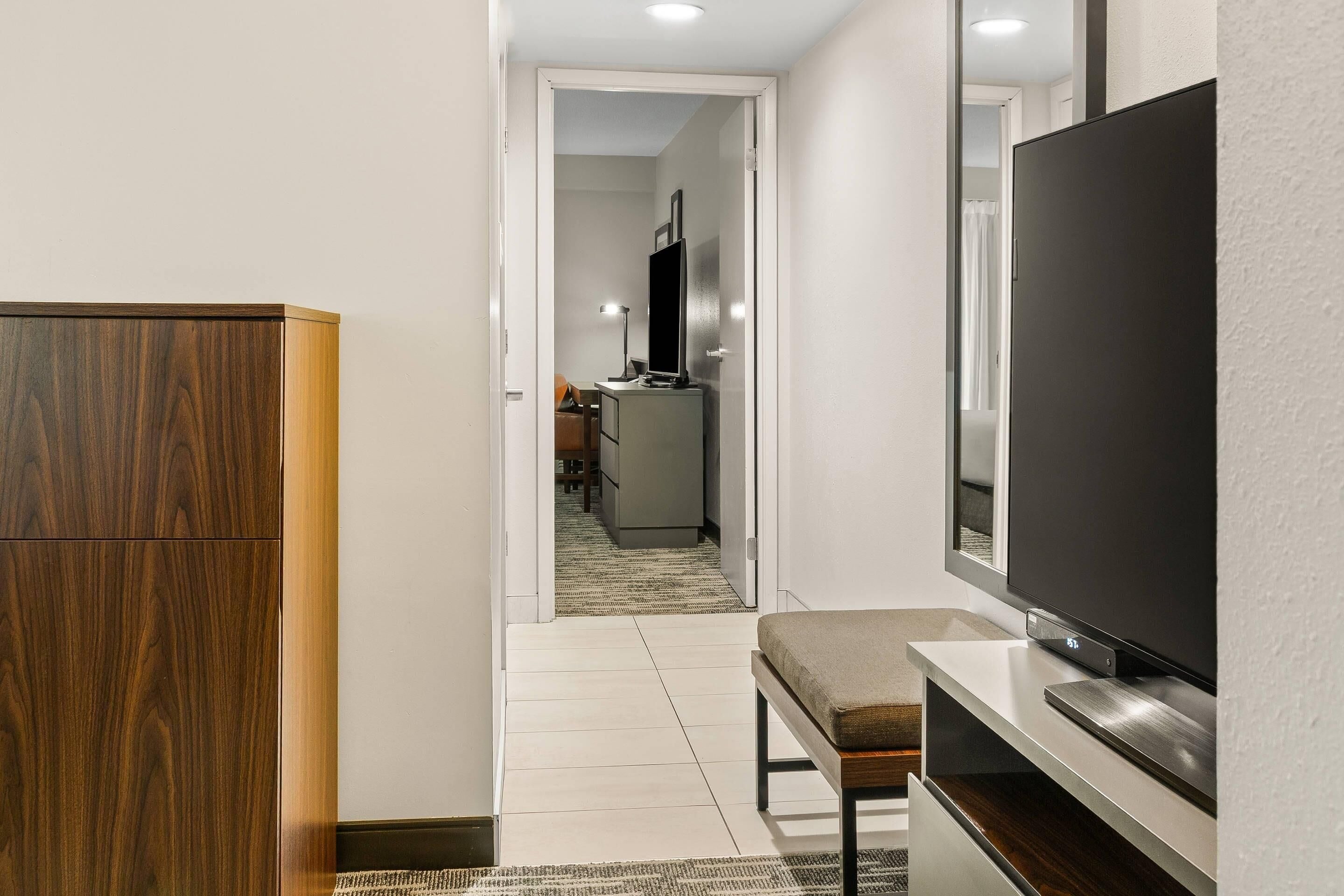 A hallway with a wooden cabinet, a bench, and a TV on a stand.