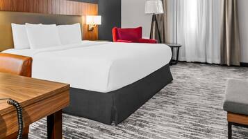 A hotel room with a large bed, a red chair, a small table, and a lamp.