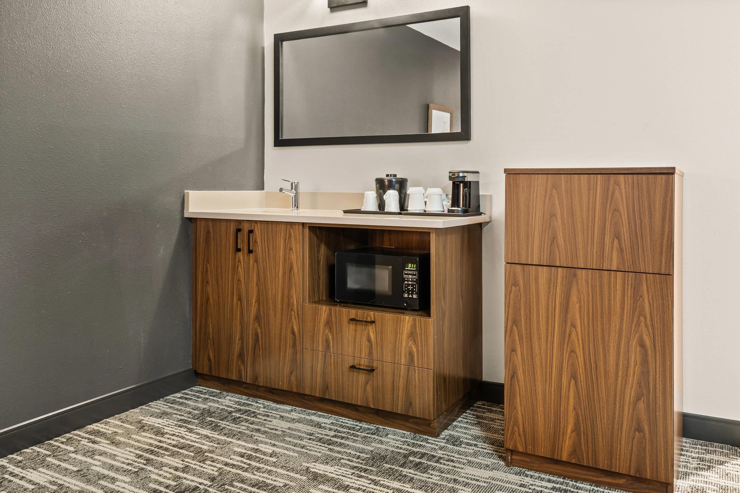Une salle de bain avec un meuble-lavabo en bois, un four à micro-ondes, une machine à café et un miroir.