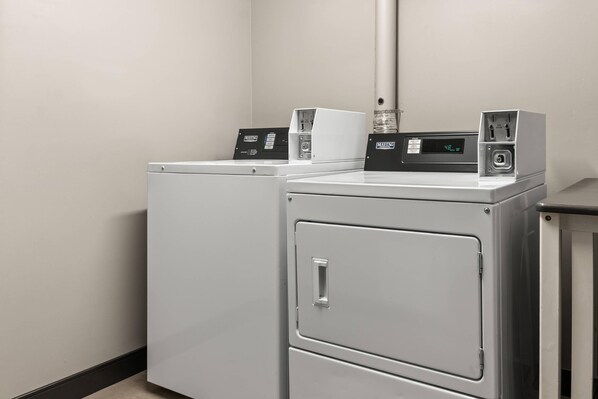 A laundry room with two white washing machines and a dryer, equipped with control panels and a digital display.