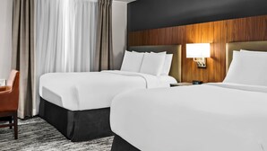 A hotel room with two beds, a wooden headboard, a nightstand with a lamp, and a chair.