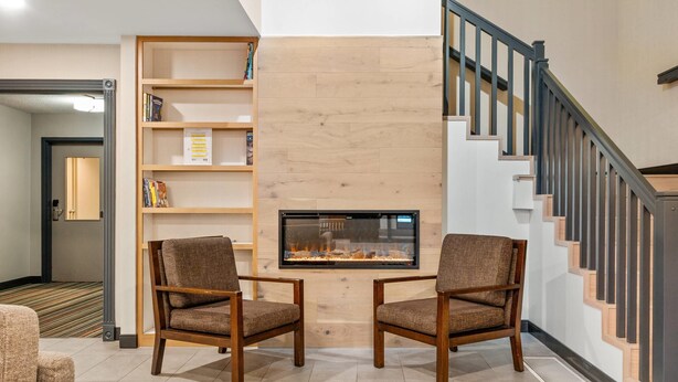 A modern living room with a fireplace, two armchairs, a bookshelf, and a staircase.