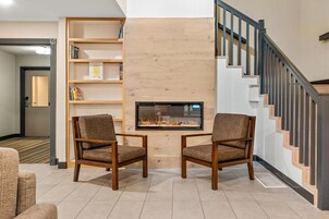 A modern living room with a fireplace, two armchairs, a bookshelf, and a staircase.