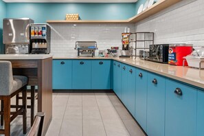 A modern kitchen with blue cabinets, a coffee machine, a toaster, and a red container of food.