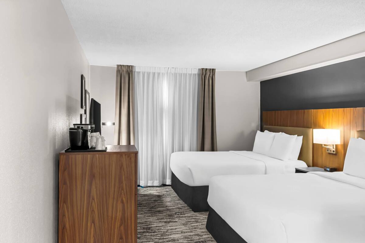 A hotel room with two beds, a wooden desk, a television, and a lamp.