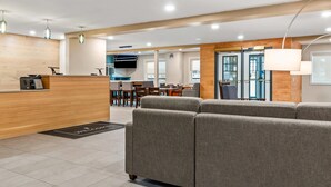 A modern hotel lobby with a reception desk, seating area, and a dining space.