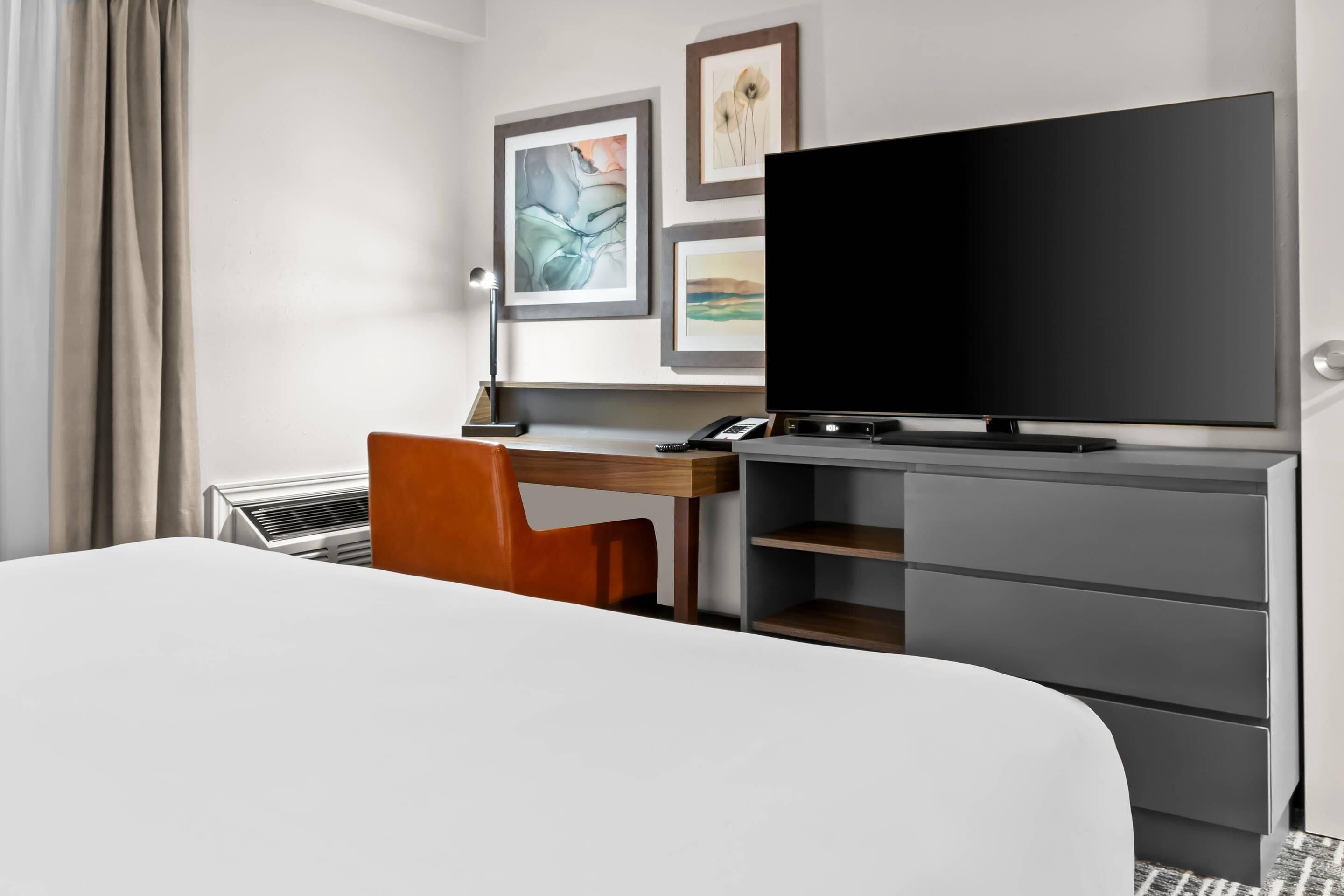 A hotel room with a bed, a desk with a chair, a television, and a wardrobe.