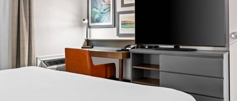 A hotel room with a bed, a desk with a chair, a television, and a wardrobe.
