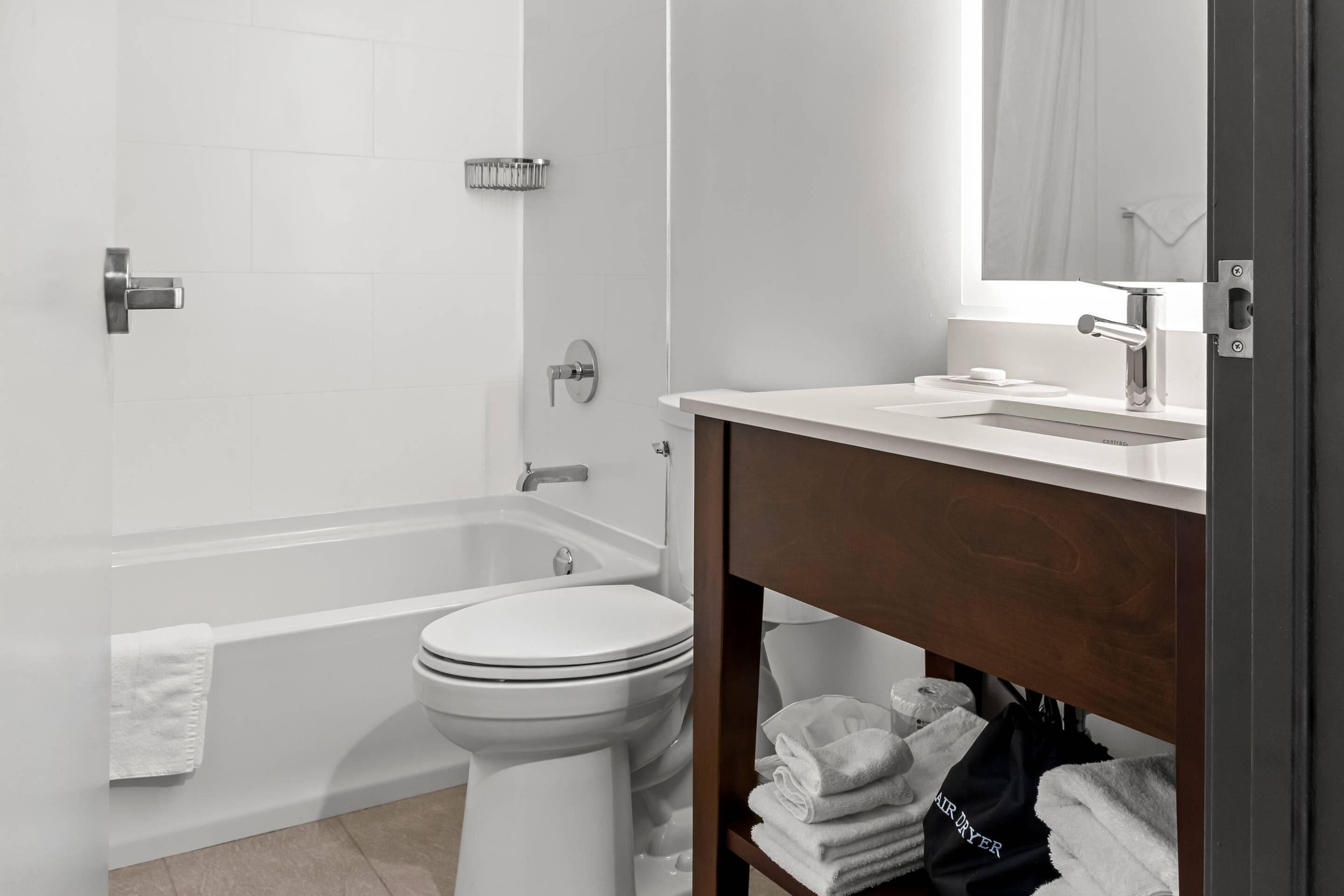 A modern bathroom with a white toilet, a bathtub, and a vanity with a mirror.