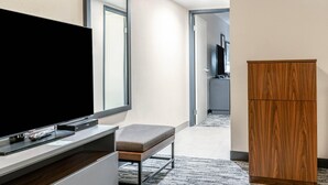 A hotel room with a flat-screen TV on a stand, a wooden cabinet, and a bench.