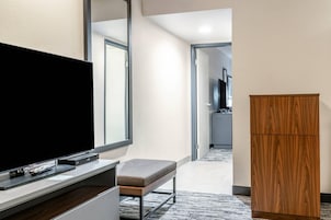 A hotel room with a flat-screen TV on a stand, a wooden cabinet, and a bench.