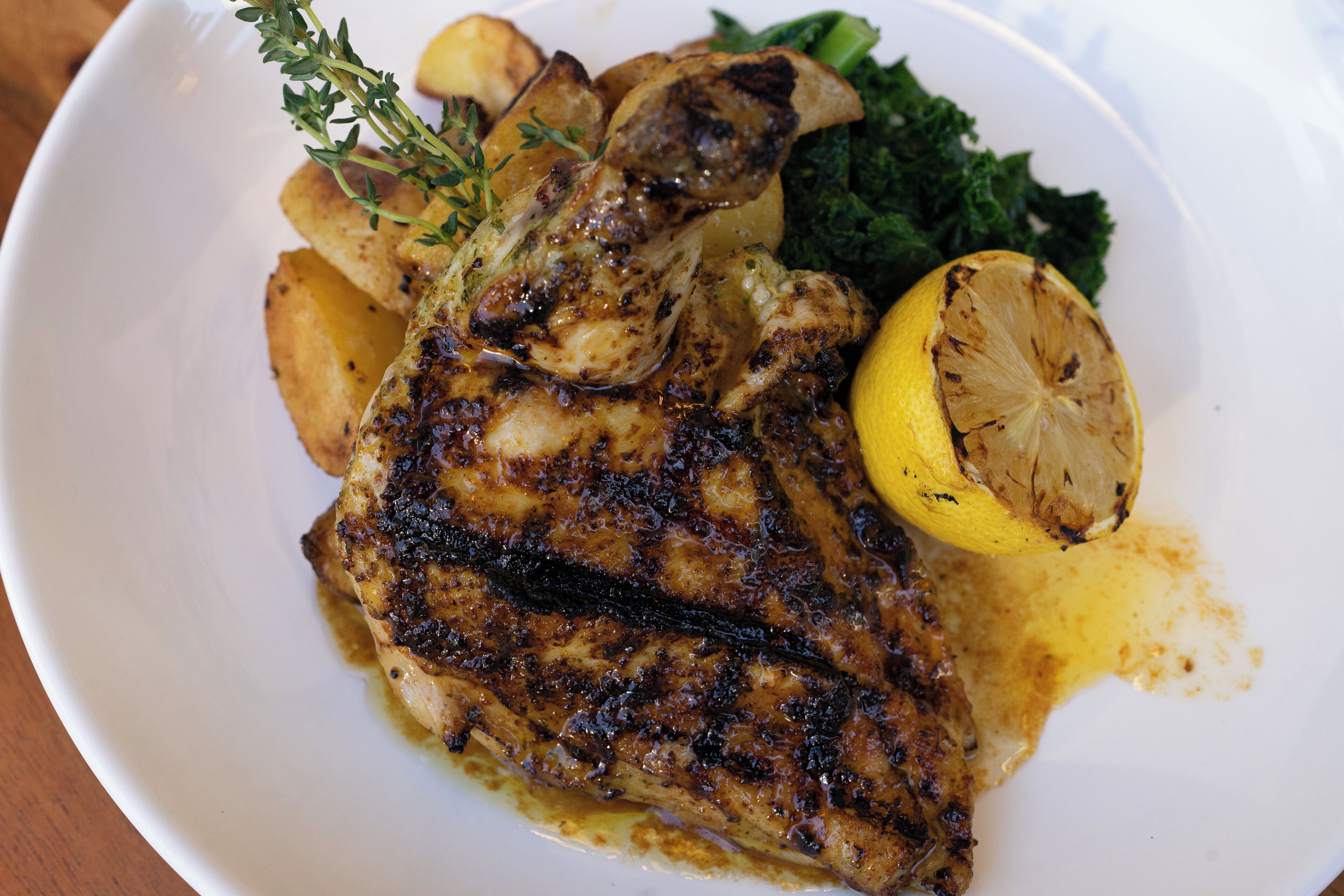 A plate with grilled chicken, roasted potatoes, and a slice of lemon.