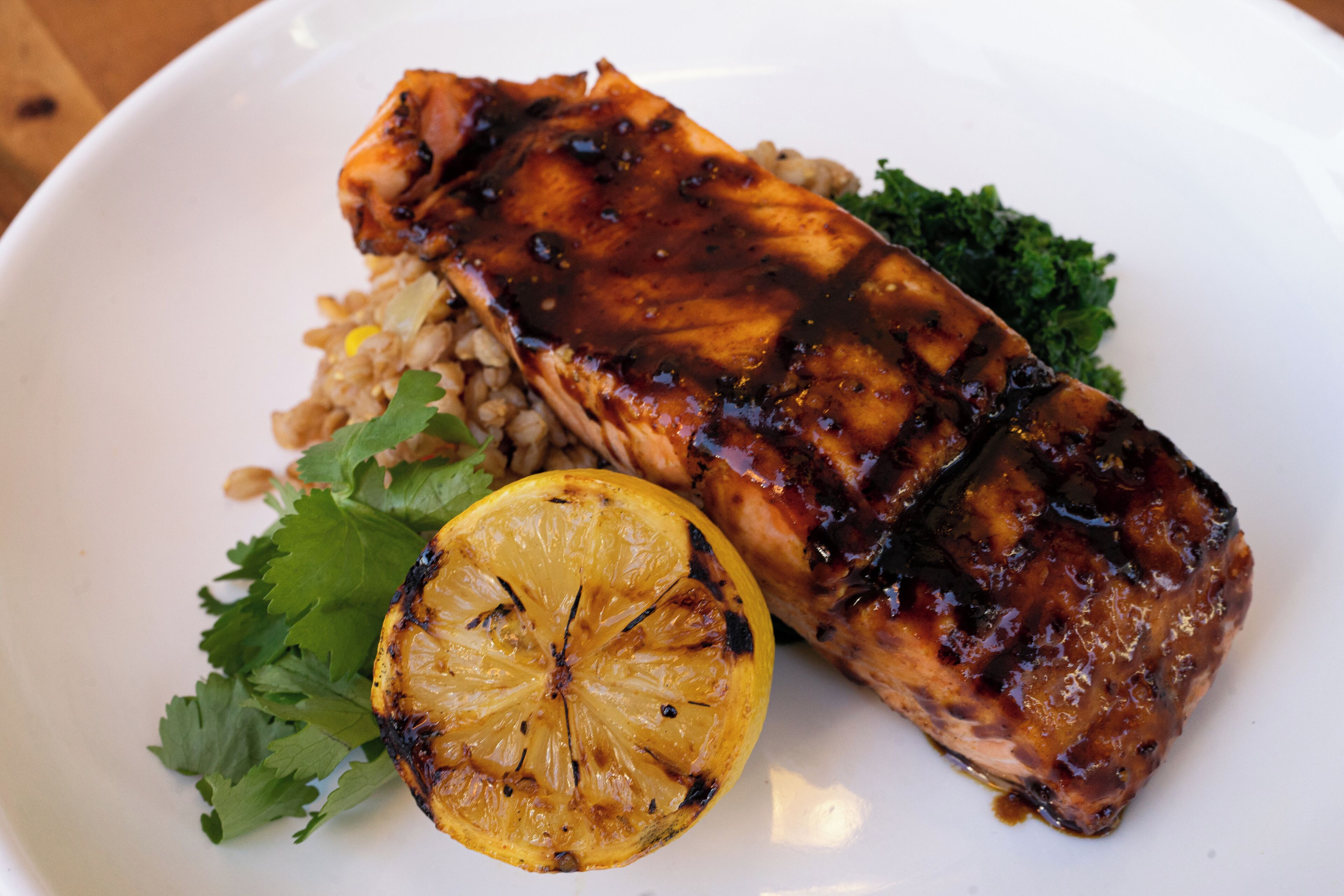 A plate with grilled salmon, a slice of lemon, and some greens.