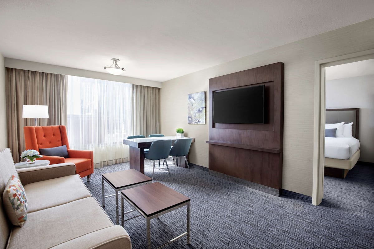 A hotel room with a sofa, armchair, coffee table, TV, dining area, and a bed.