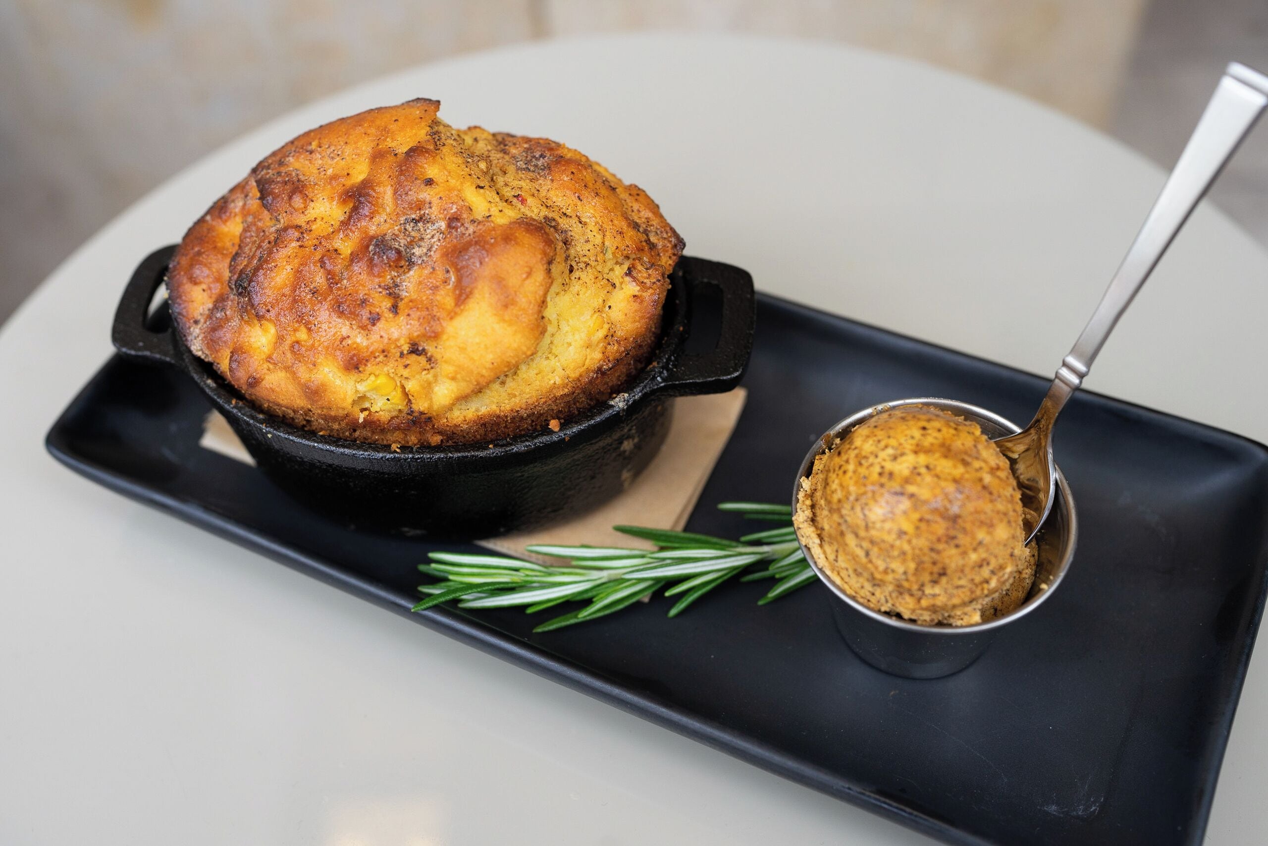 A cast iron skillet with a baked dish and a spoonful of sauce on a black tray.