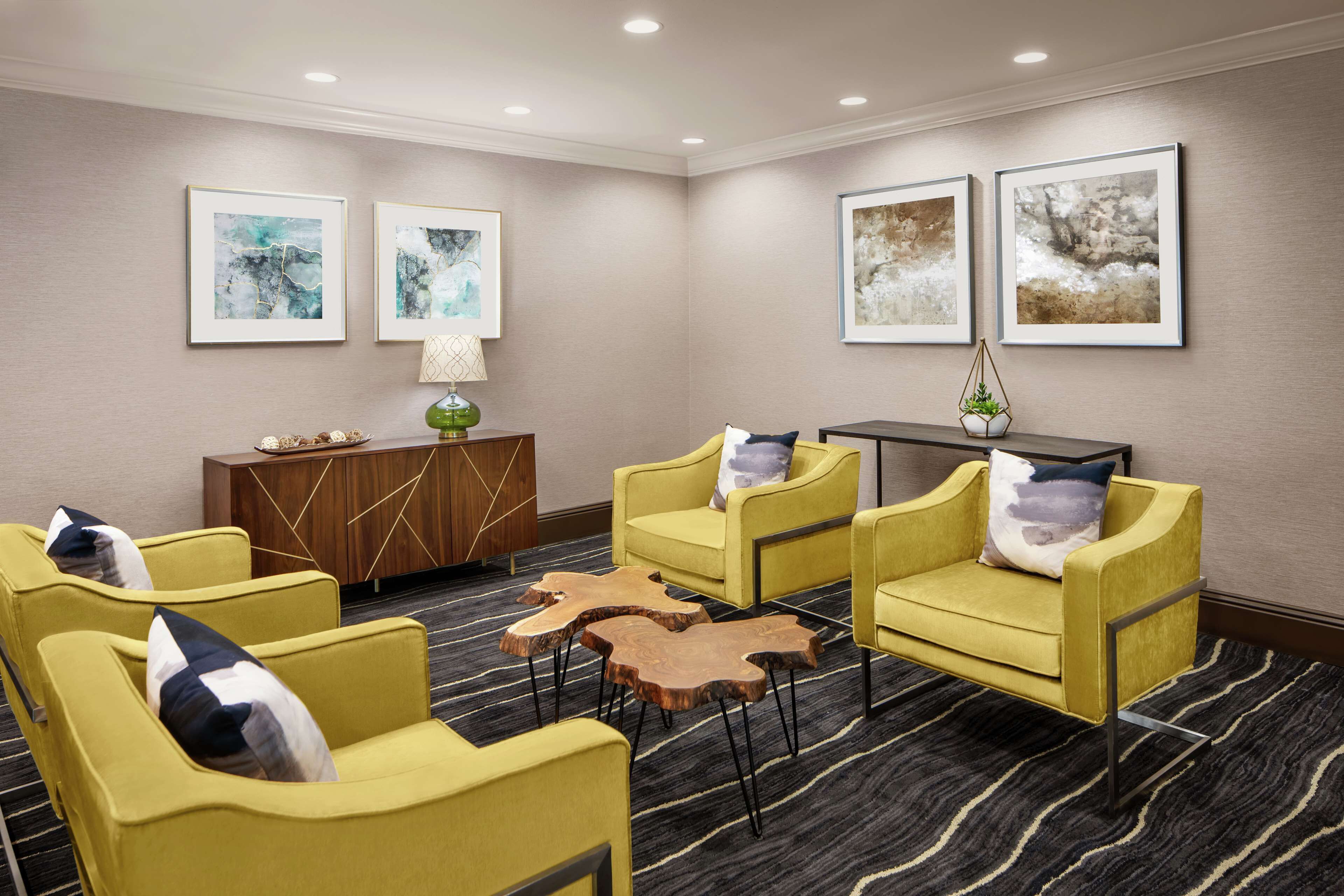 Quarto de hotel com área de estar, com poltronas amarelas, mesa de centro de madeira e um aparador com objetos decorativos.
