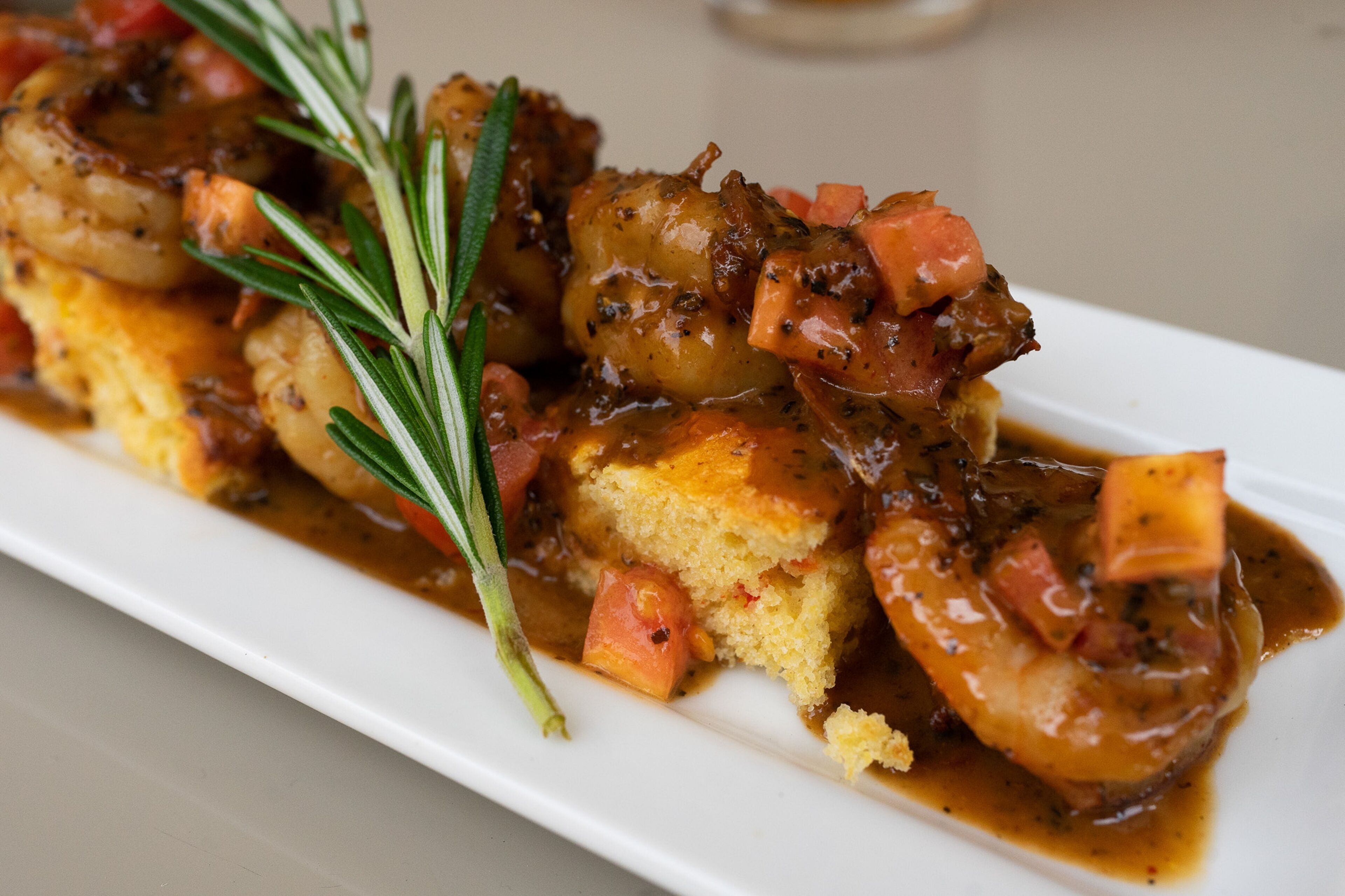 A dish with shrimp, diced tomatoes, and a garnish of rosemary.