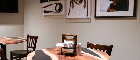 A dining area with round tables and chairs, a coffee machine, and framed artwork on the walls.