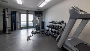 A gym with a treadmill, dumbbells, and weight machines.