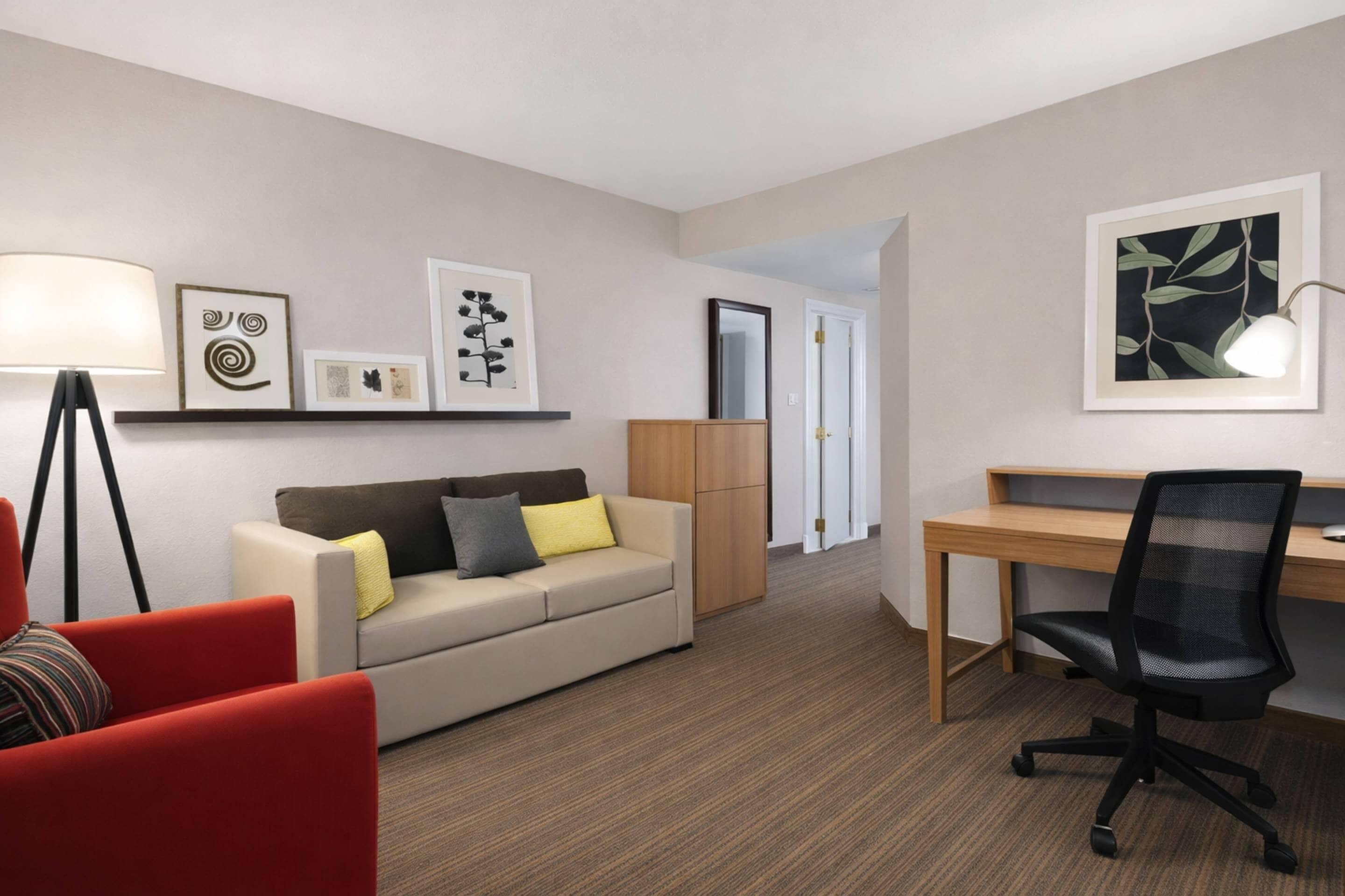 A hotel room with a sofa, a desk, a chair, a lamp, and artwork on the walls.