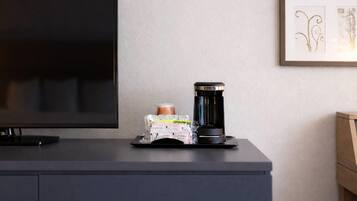 A flat-screen TV on a dark-colored cabinet, a coffee maker, and a framed artwork on the wall.