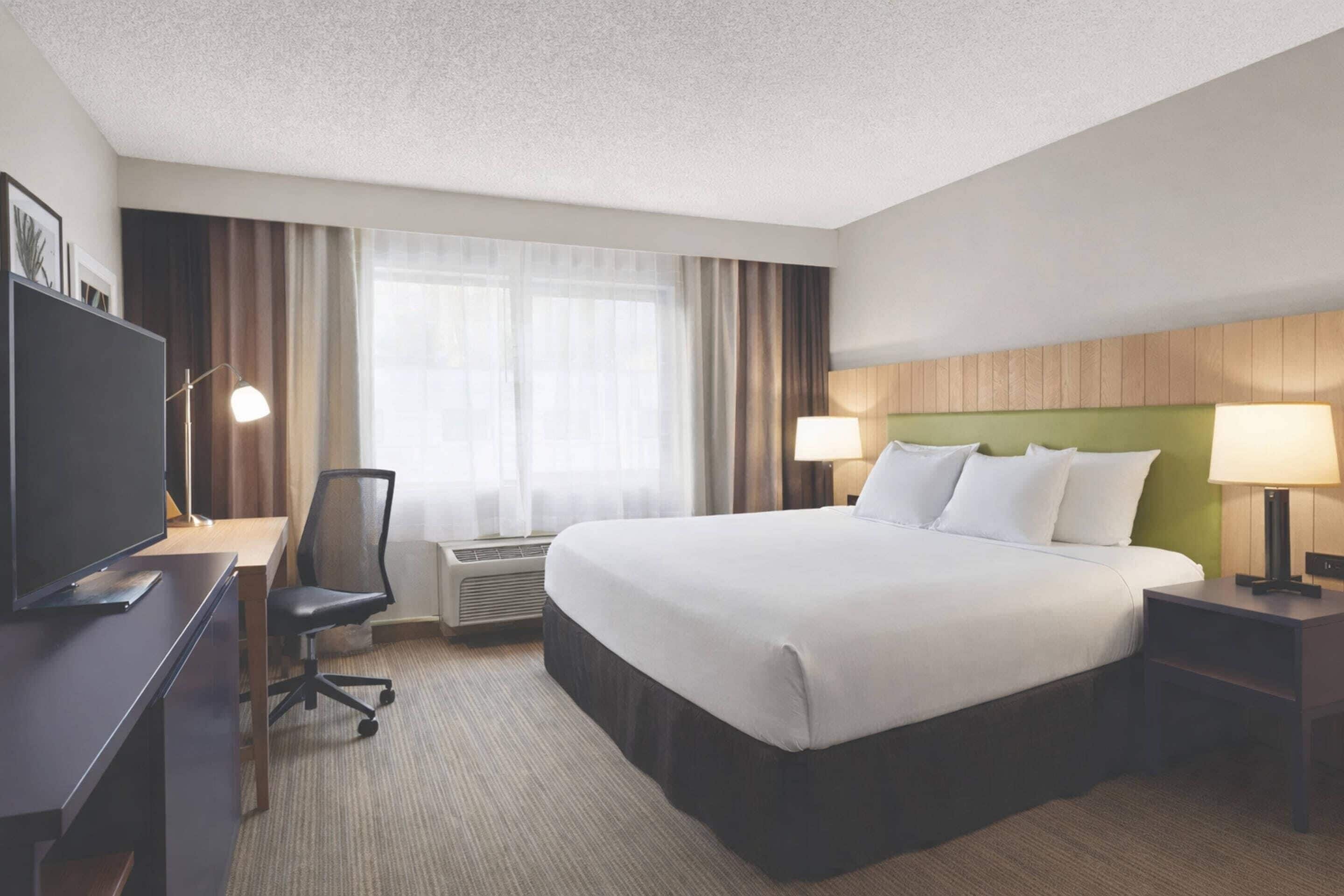 A hotel room with a large bed, a desk with a chair, a television, and a window with curtains.