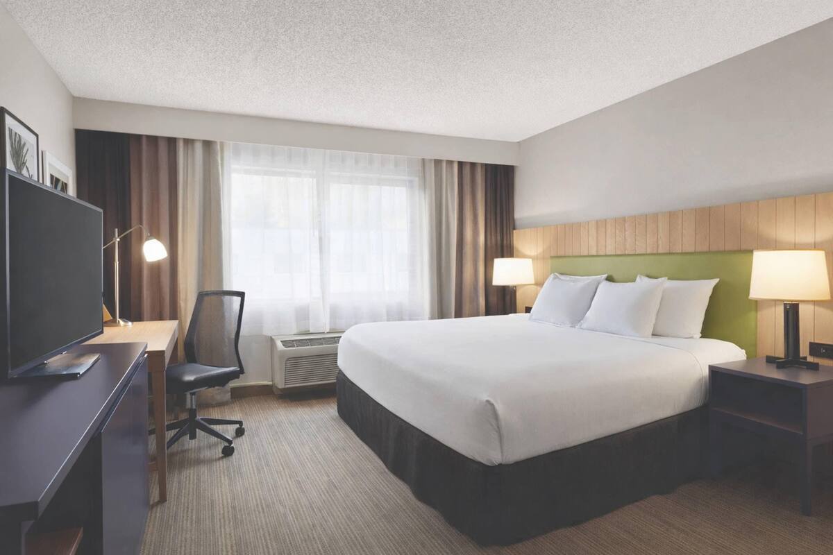 A hotel room with a large bed, a desk with a chair, a television, and a window with curtains.