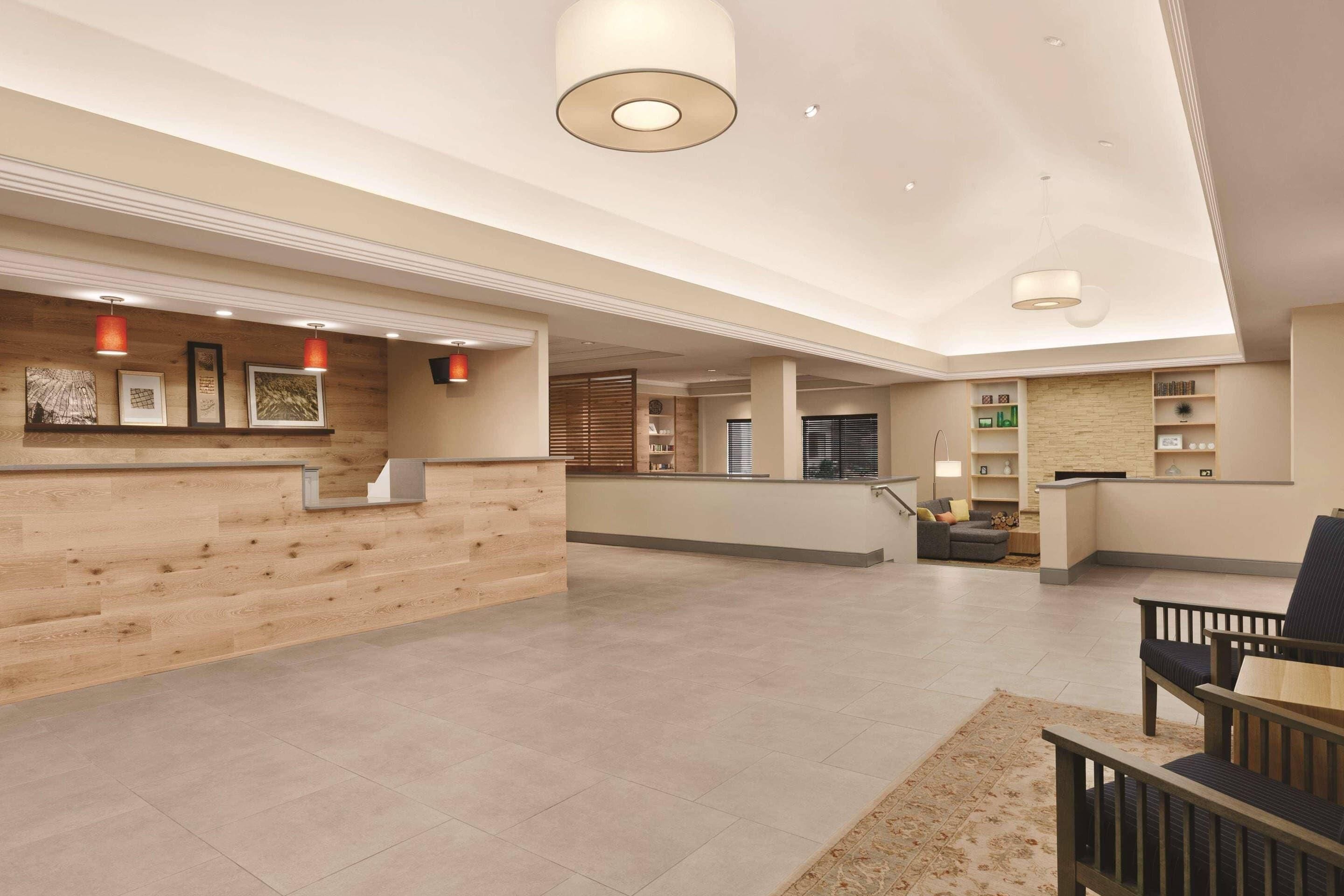 A spacious lobby with a wooden reception desk, seating area, and a staircase leading to upper floors.