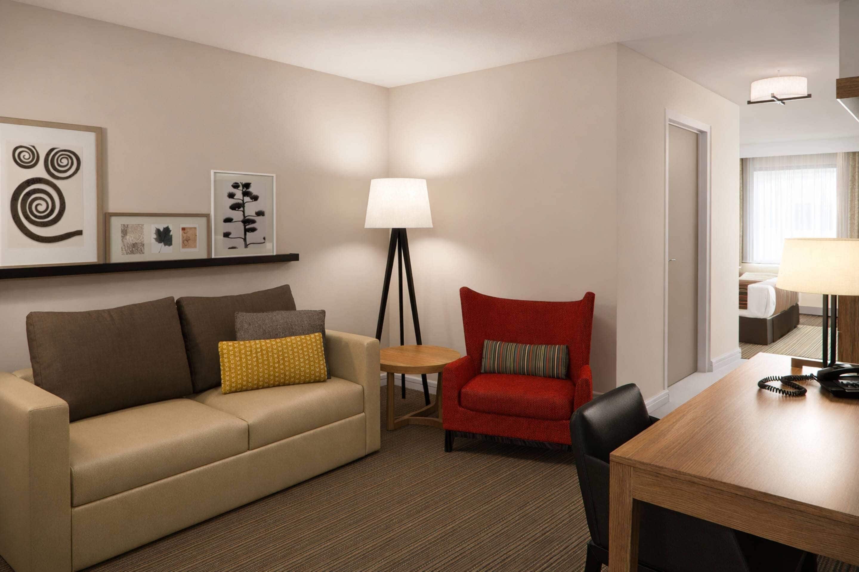 Une chambre d’hôtel équipée d’un canapé, d’un fauteuil, d’une petite table, d’une lampe et d’une table à manger avec un téléphone.