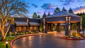 A modern hotel with a covered entrance, landscaped gardens, and a well-lit facade.