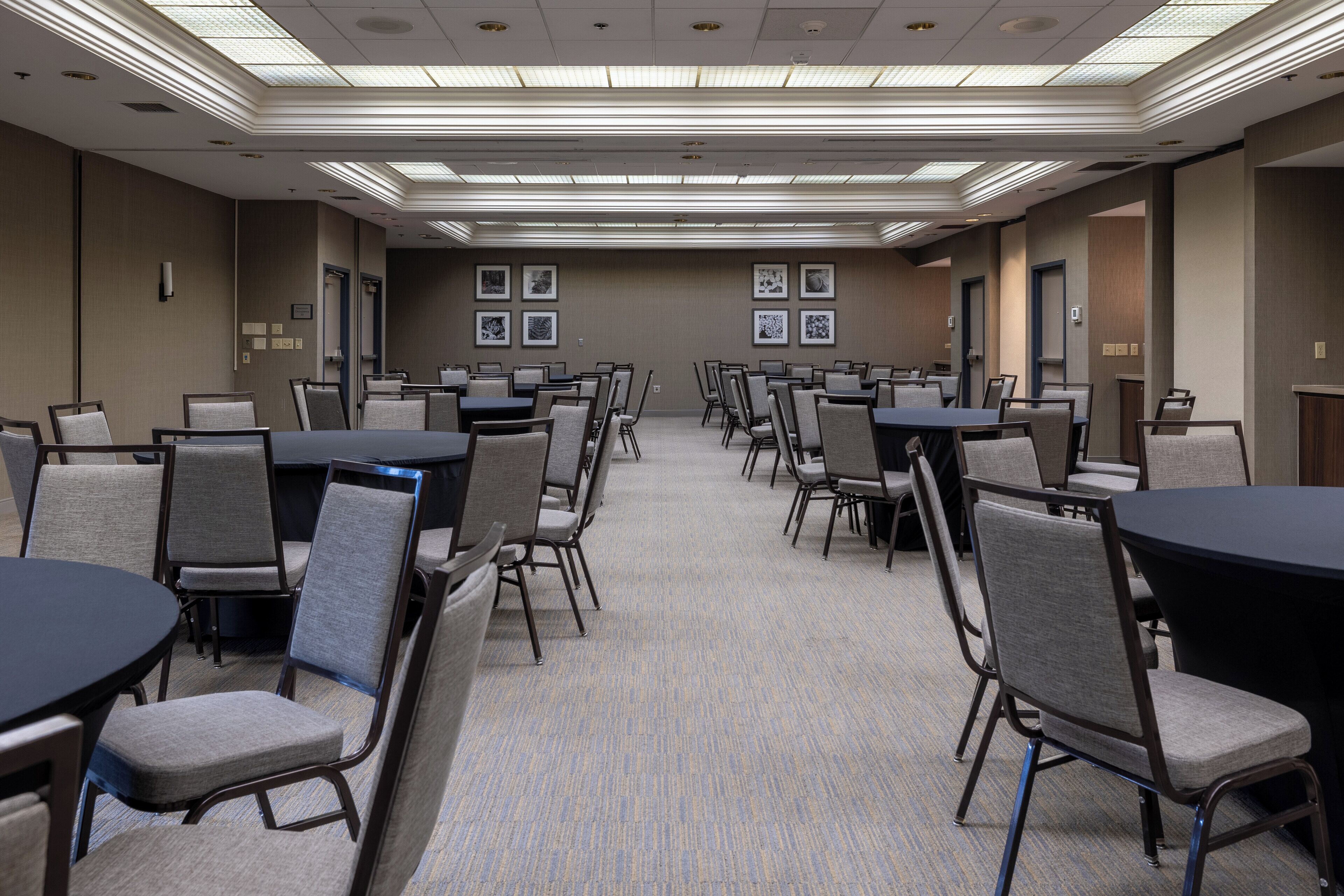 A conference room with multiple tables and chairs, recessed ceiling lighting, and framed pictures on the walls.