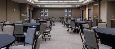 A conference room with multiple tables and chairs, recessed ceiling lighting, and framed pictures on the walls.