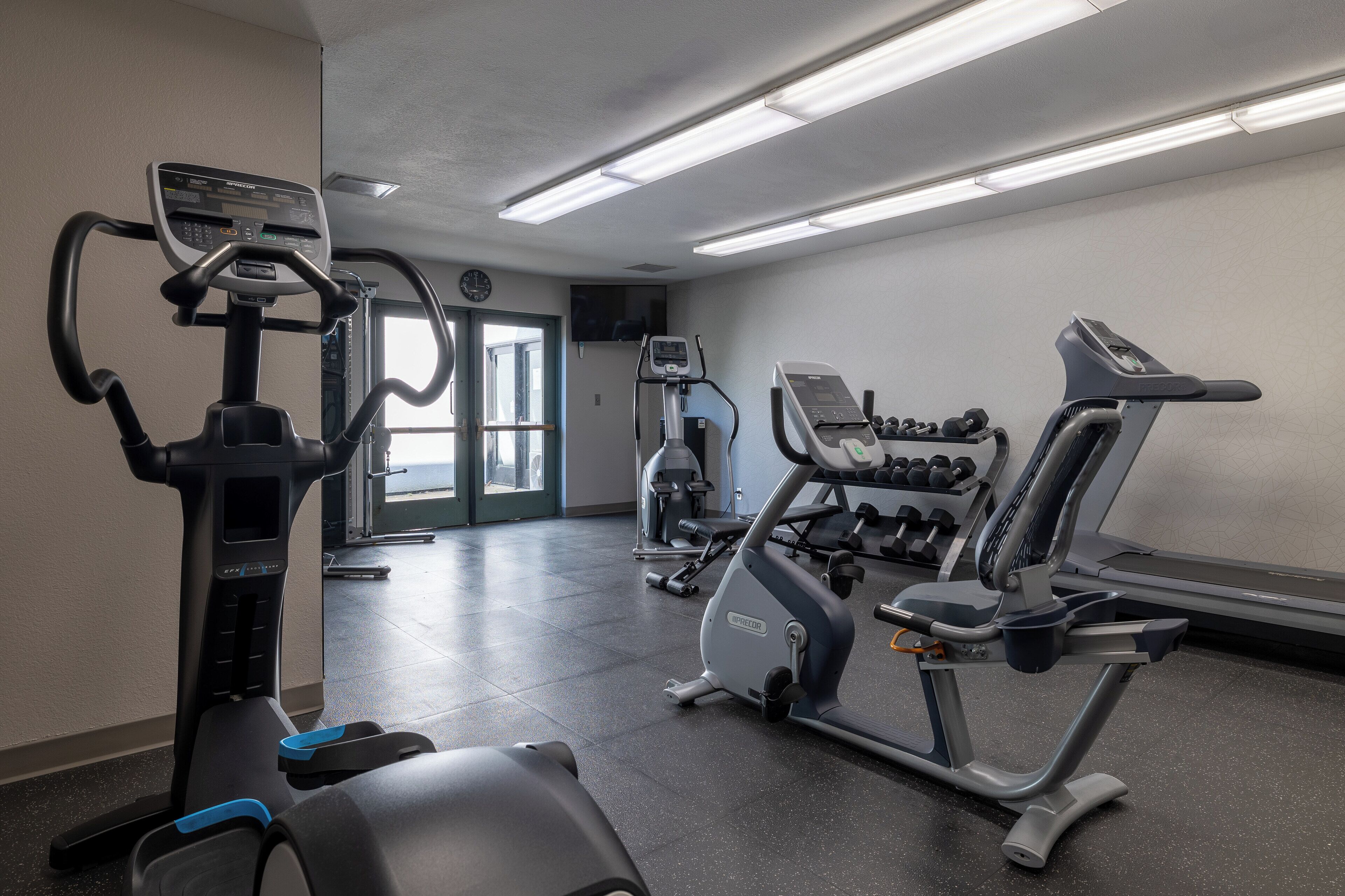 A gym with various exercise equipment including treadmills, an elliptical, and dumbbells.