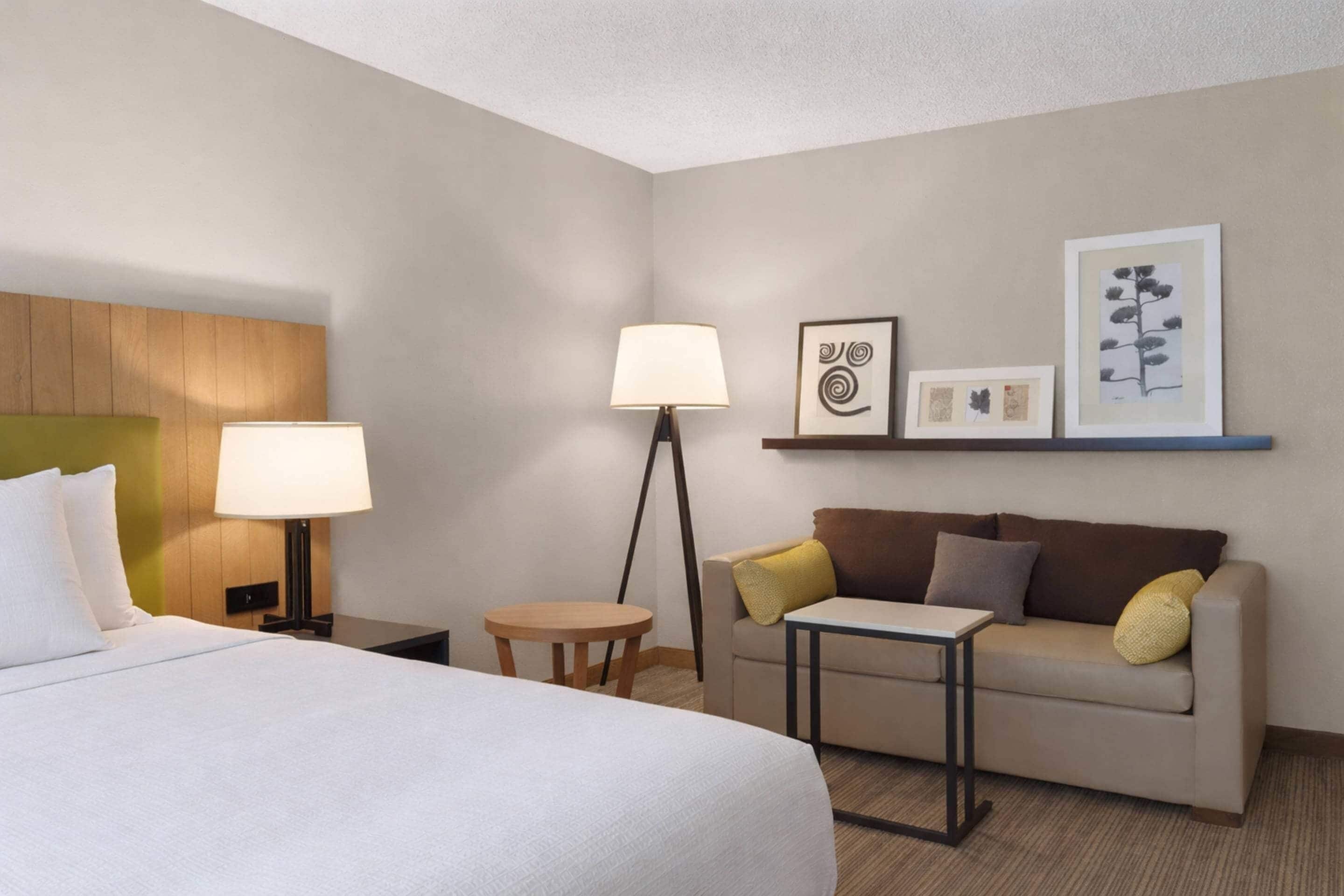 Una habitación de hotel con cama, sofá, una mesita, lámpara y decoración en la pared.