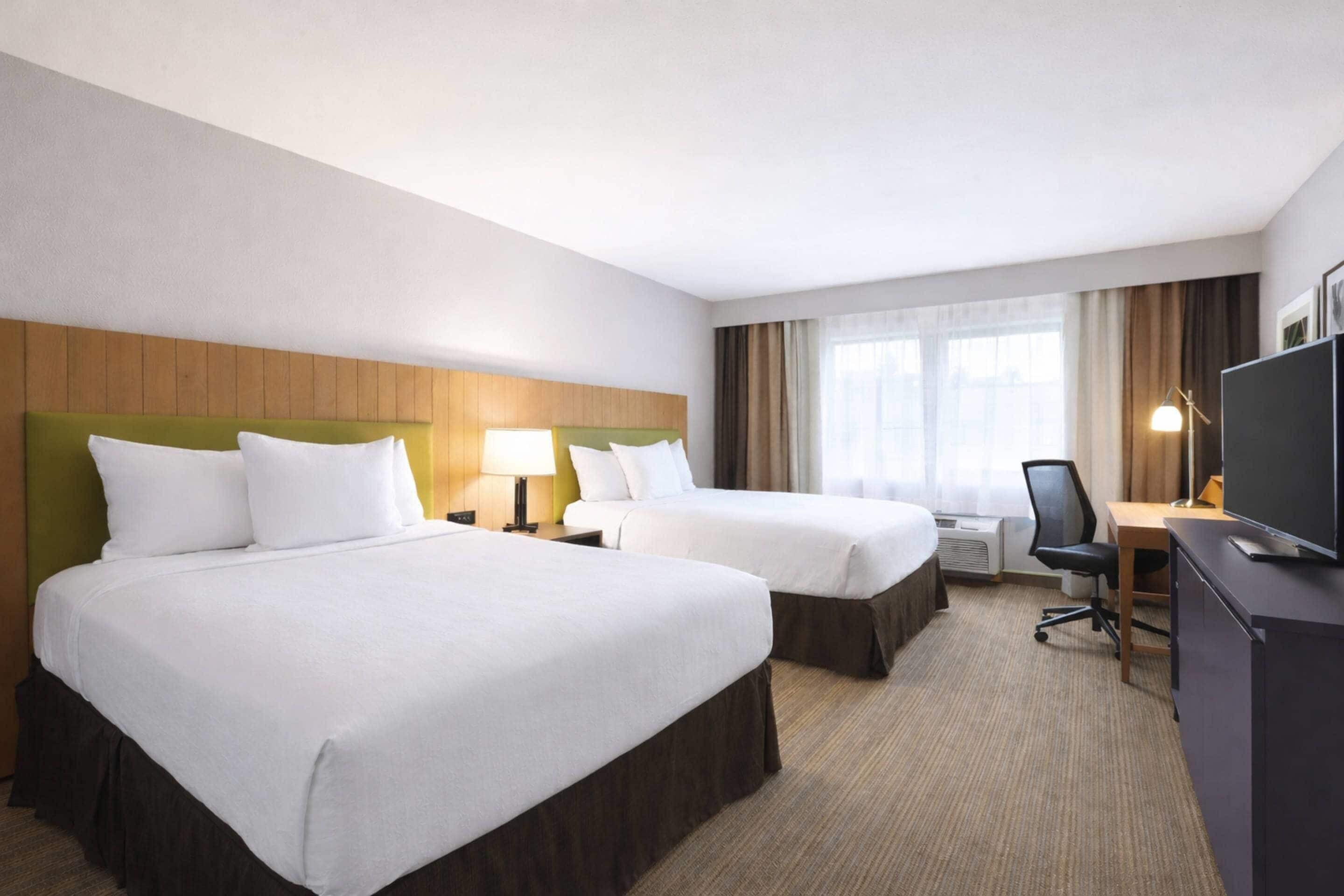 A hotel room with two beds, a desk, a chair, a TV, and a window with curtains.
