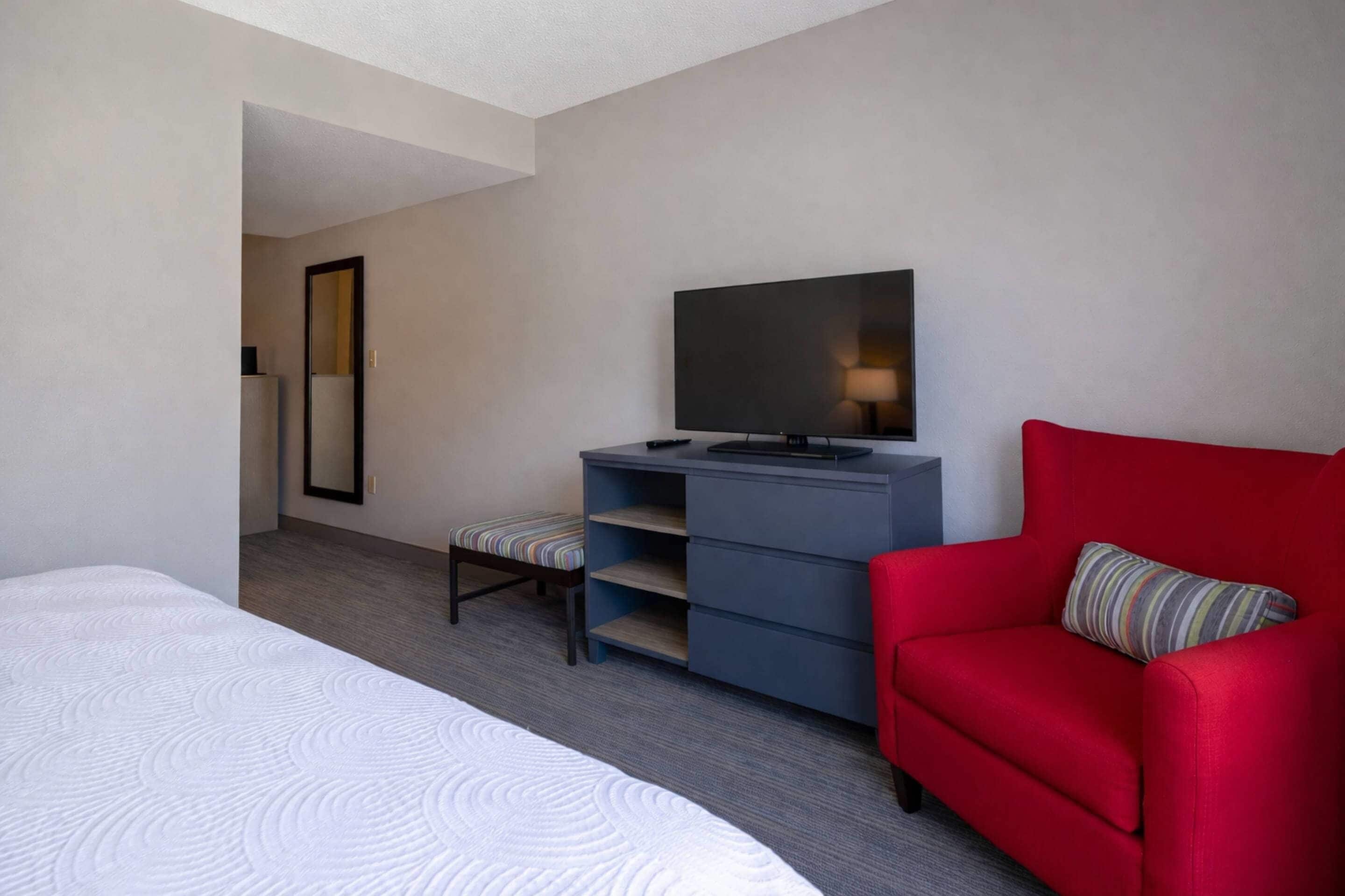 Una habitación de hotel con una cama, un sofá rojo, un televisor, un espejo y una pequeña mesa.