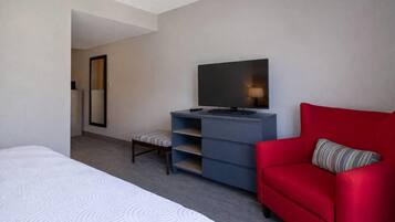Una habitación de hotel con una cama, un sofá rojo, un televisor, un espejo y una pequeña mesa.